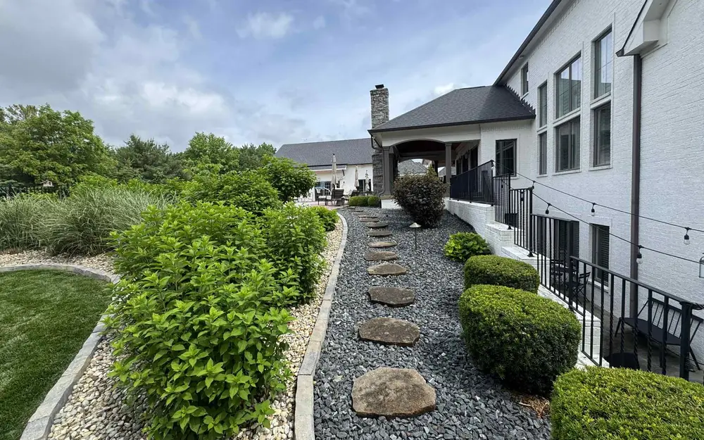 Residential landscape design with stepping stone path, river rock beds and trimmed shrubs by PMT Lawn & Landscape